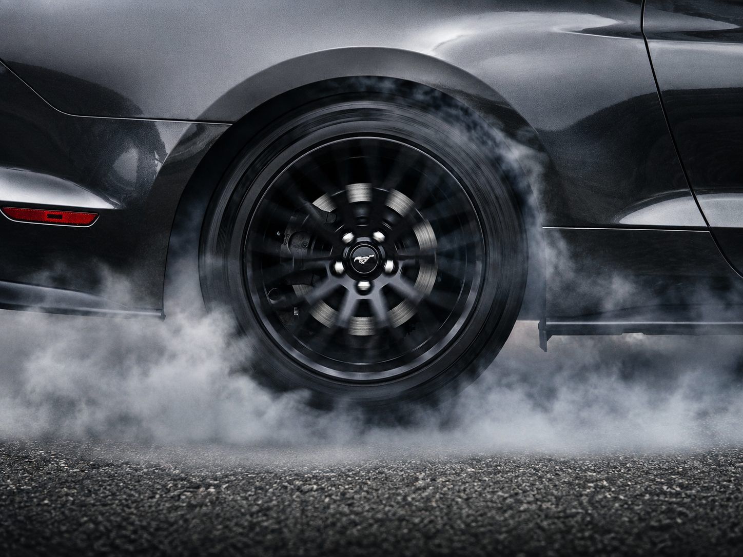 Ford Mustang GT mid-burnout, rear wheel wrapped in tire smoke